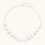 Graduated pearl-finish silver discs forming an organic bubble bib necklace on delicate chain against cream background.