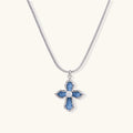 Blue denim-inlaid cross pendant with white gold frame and center zirconia on silver snake chain against cream background