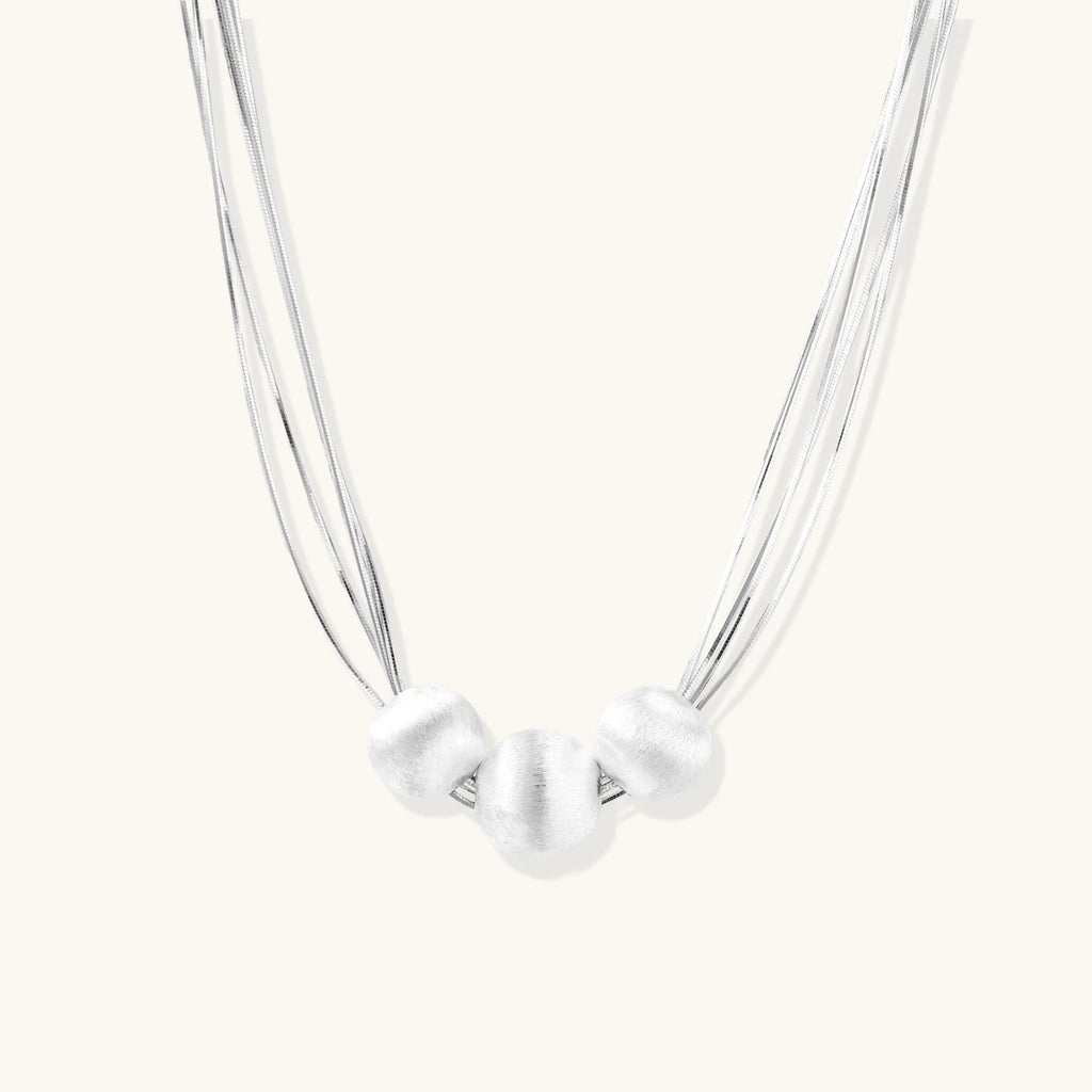 Sterling silver multi-strand necklace with three brushed round beads on cream background