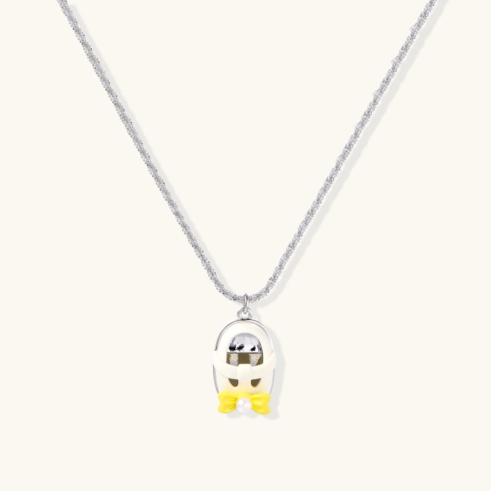 Chrome egg-shaped pendant with kawaii face, yellow bow, and pearl detail on silver chain against white background