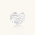 Wide sterling silver cuff ring with flowing wave patterns creating dimensional texture against cream background