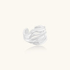 Wide sterling silver cuff ring with flowing wave patterns creating dimensional texture against cream background