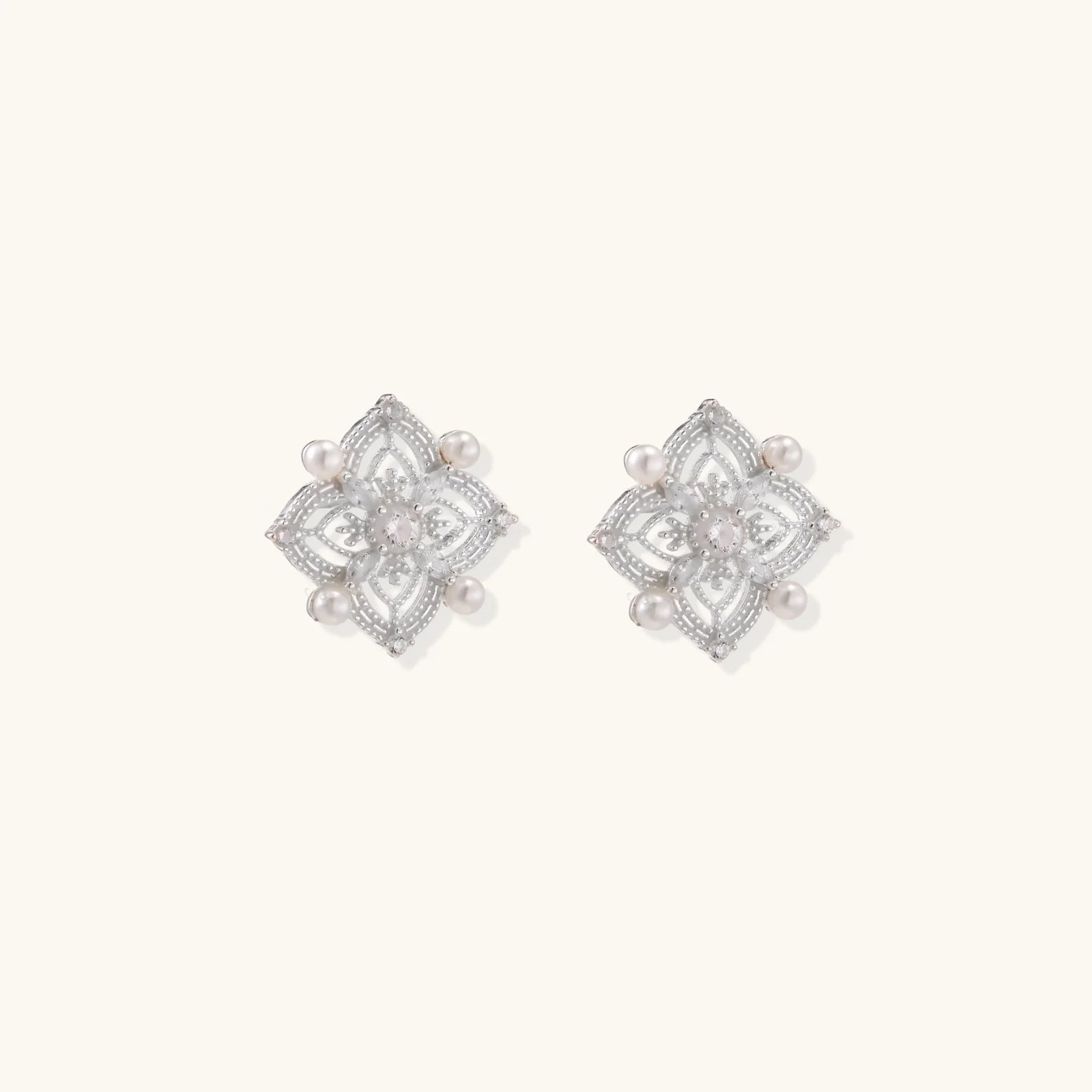 Ornate sterling silver stud earrings with mandala-inspired filigree pattern and four freshwater pearls on beige background