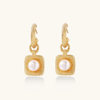 Pair of gold vermeil hoop earrings with textured square frames holding freshwater pearls on cream background