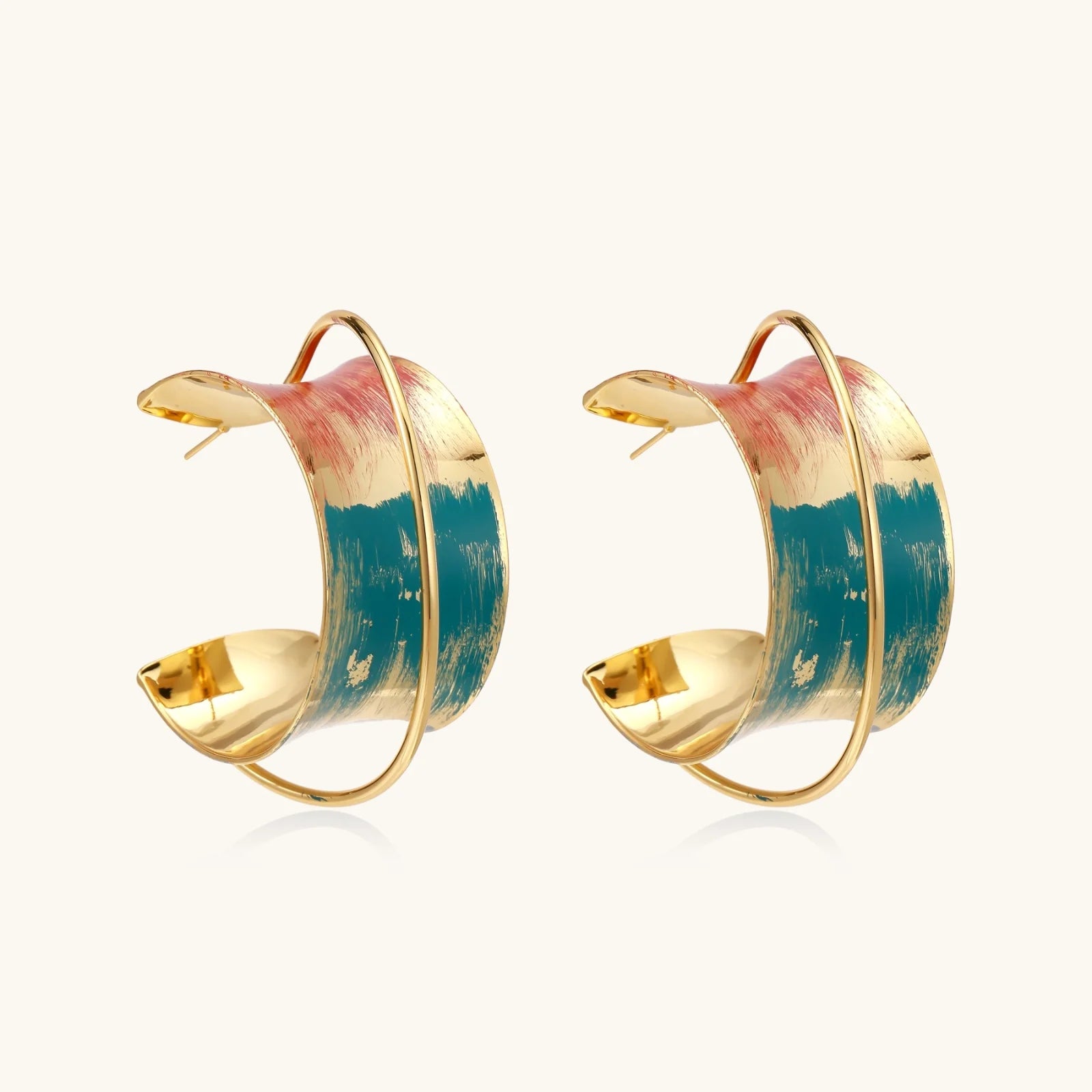 Gold-plated hoop earrings with teal and coral enamel brushstroke design on cream background