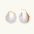 Shell-shaped hoop earrings with iridescent blue-pink enamel and gold trim on cream background