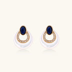 Gold drop earrings with oval lapis lazuli, crystal-paved frame, and iridescent mother-of-pearl teardrop on cream background