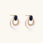 Gold drop earrings with oval lapis lazuli, crystal-paved frame, and iridescent mother-of-pearl teardrop on cream background