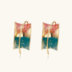 Gold-plated hoop earrings with teal and coral enamel brushstroke design on cream background