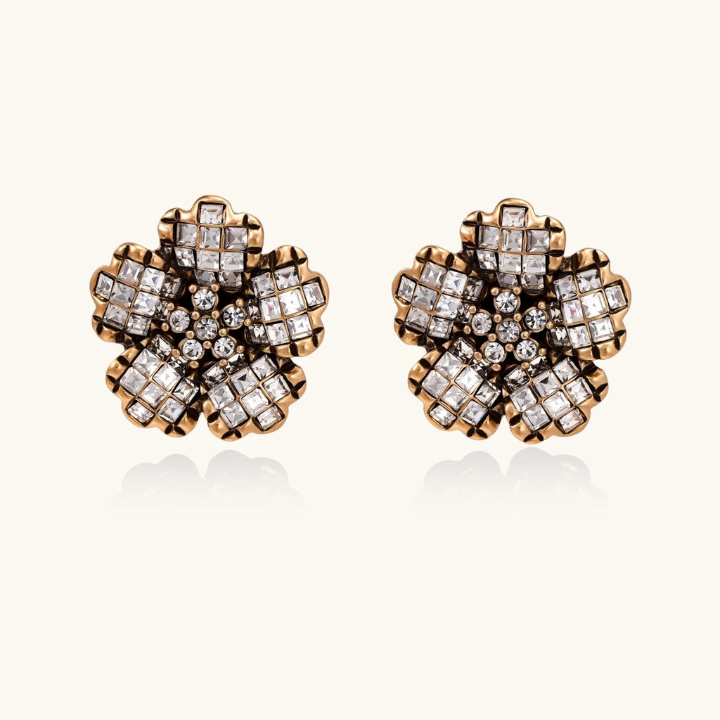 Gold-plated floral stud earrings with geometric zirconia crystals arranged in five-petal design on cream background