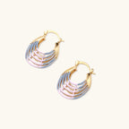 Gold hoop earrings with gradient blue-to-pink enamel in ribbed fan design on beige background