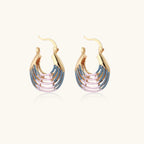 Gold hoop earrings with gradient blue-to-pink enamel in ribbed fan design on beige background