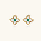 Gold quatrefoil stud earrings with white mother-of-pearl petals and emerald green gemstone center on beige background.