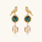 Gold-plated bird stud earrings with iridescent abalone shell medallions and champagne crystal drops on cream background