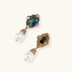 Ornate gold-plated earrings with iridescent abalone shell, crystals, blue stones, and white pearl drops on cream background.