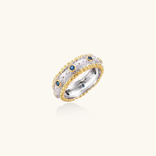 Two-tone ring with brushed silver center, gold beaded edges, and blue zirconia stones on white background.