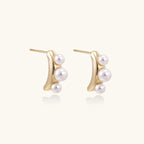 14K gold-plated curved stud earrings with three white freshwater pearls aligned vertically on cream background