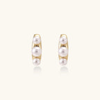 14K gold-plated curved stud earrings with three white freshwater pearls aligned vertically on cream background
