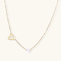 Delicate gold necklace with open heart charm and white pearl bead on fine chain against cream background