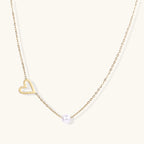 Delicate gold necklace with open heart charm and white pearl bead on fine chain against cream background