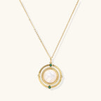 Gold pendant necklace with circular orbital design, iridescent mother-of-pearl center, and green zirconia accents