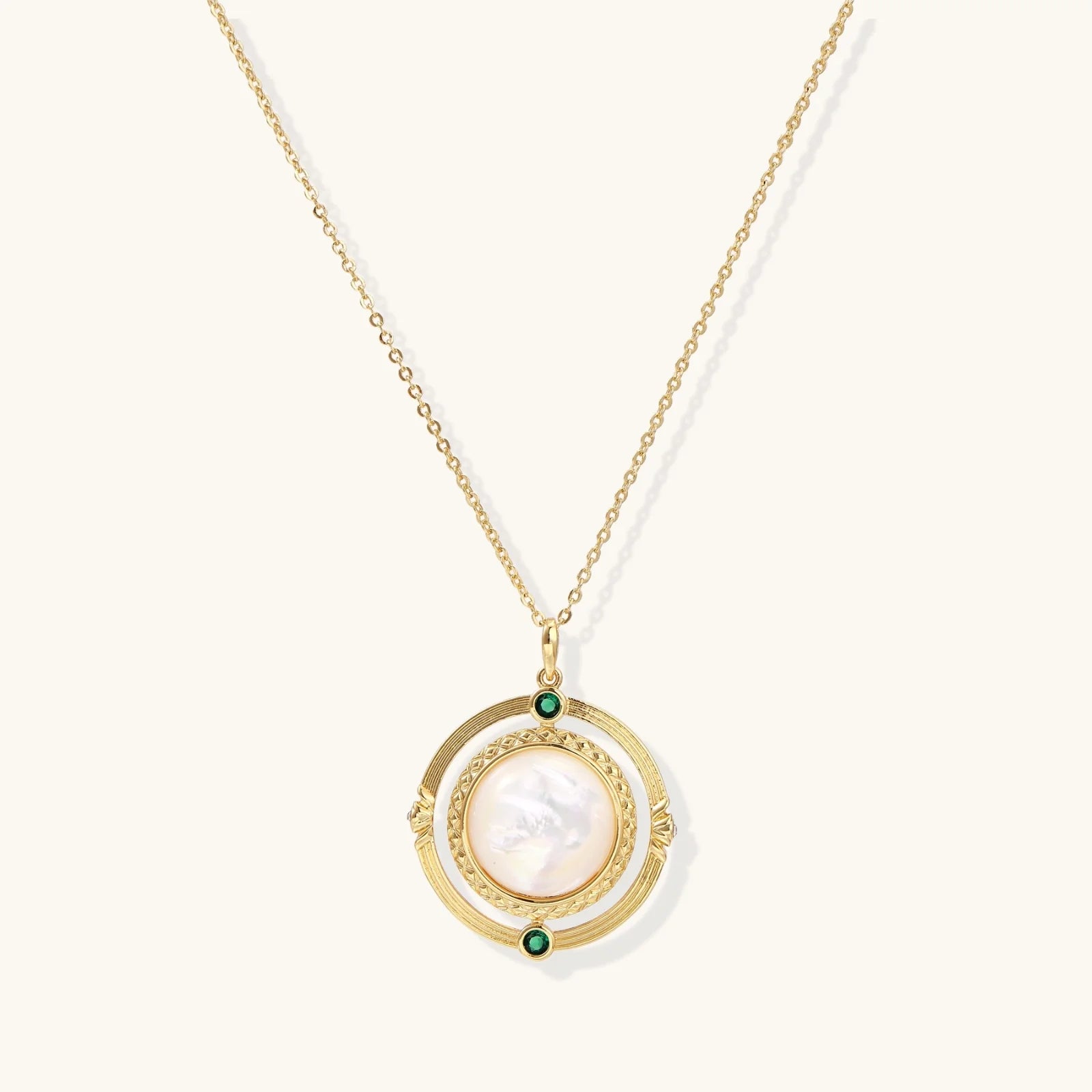 Gold pendant necklace with circular orbital design, iridescent mother-of-pearl center, and green zirconia accents