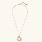Gold pendant necklace with circular orbital design, iridescent mother-of-pearl center, and green zirconia accents