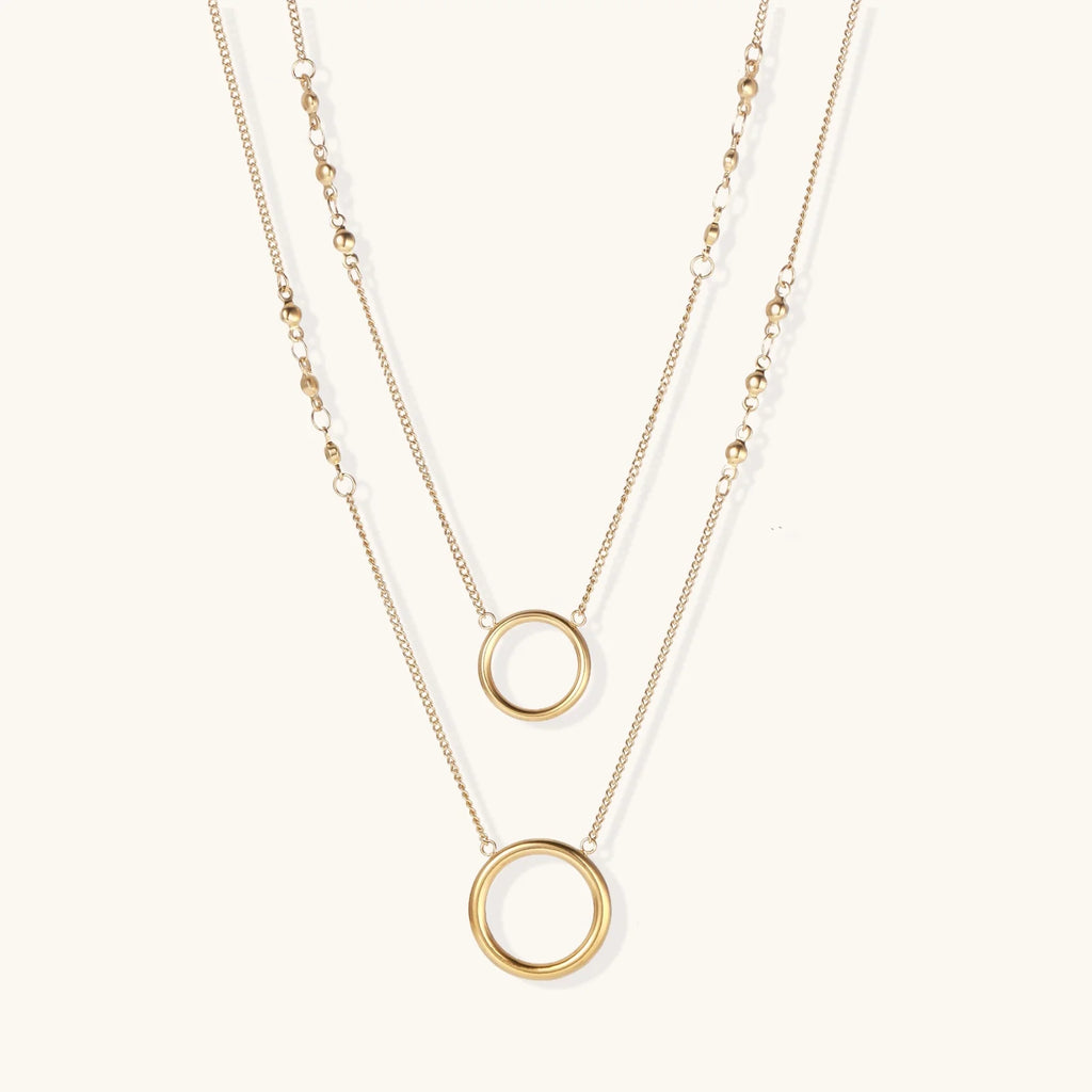 Layered gold necklace set with two open circle pendants and mixed chain styles on beige background