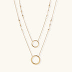 Layered gold necklace set with two open circle pendants and mixed chain styles on beige background