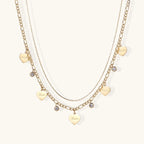 Gold layered necklace set with engraved heart pendants and crystal accents on cream background