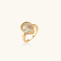 Teardrop-shaped gold-plated ring with turquoise enamel flowers and crystal pavé detail on cream background
