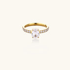 Gold-plated solitaire ring with oval zirconia center stone and pavé band on cream background
