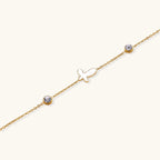 Gold chain bracelet with white mother of pearl butterfly pendant and two bezel-set crystals on cream background