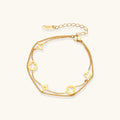 Double-layer gold-plated bracelet with quatrefoil and star charms on cream background, 18K gold finish.