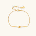 Delicate gold chain bracelet with minimalist bar and centered knot detail on cream background