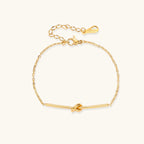Delicate gold chain bracelet with minimalist bar and centered knot detail on cream background