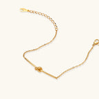 Delicate gold chain bracelet with minimalist bar and centered knot detail on cream background