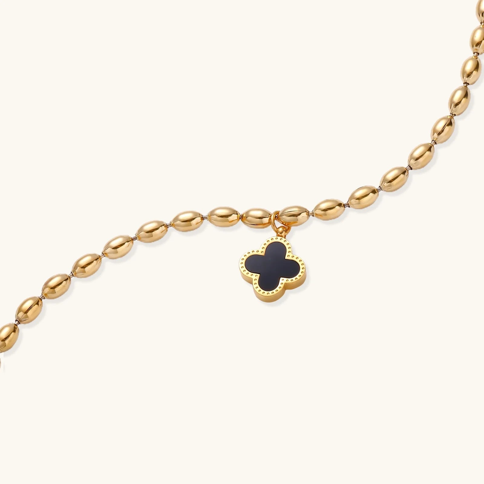 18K gold-plated oval bead chain bracelet with quatrefoil clover charm featuring mother of pearl inlay on cream background