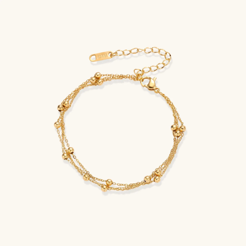 Three-strand gold-plated bracelet with clustered ball beads and adjustable clasp on cream background