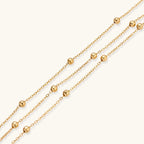 Three-strand gold-plated bracelet with clustered ball beads and adjustable clasp on cream background