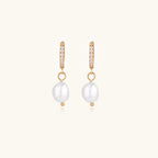 Gold huggie hoop earrings with pavé crystals and white freshwater pearl drops on cream background