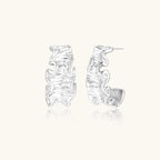 White gold plated sculptural hoop earrings with organic wavy edges and reflective metallic finish on cream background