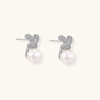 White gold plated studs featuring pavé X-shaped tops with freshwater pearl drops on cream background.