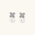 White gold plated studs featuring pavé X-shaped tops with freshwater pearl drops on cream background.