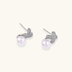 White gold plated studs featuring pavé X-shaped tops with freshwater pearl drops on cream background.