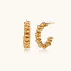 Sculptural gold-plated hoop earrings with continuous twisted spiral design on cream background