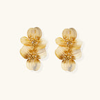 Pair of gold-plated double flower earrings with textured petals and crystal centers on cream background.