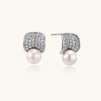 Curved pavé diamond studs in white gold-plated brass cradle lustrous freshwater pearls against cream background
