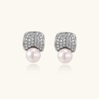 Curved pavé diamond studs in white gold-plated brass cradle lustrous freshwater pearls against cream background