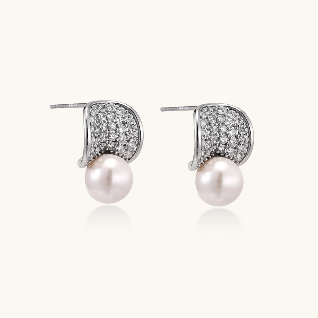 Curved pavé diamond studs in white gold-plated brass cradle lustrous freshwater pearls against cream background